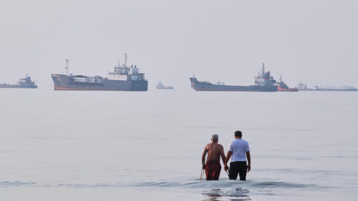 Two men wade in the waters of the Strait of Hormuz with vessels anchored in the background, off Bandar Abbas, Iran, Sunday, July 12, 2026.