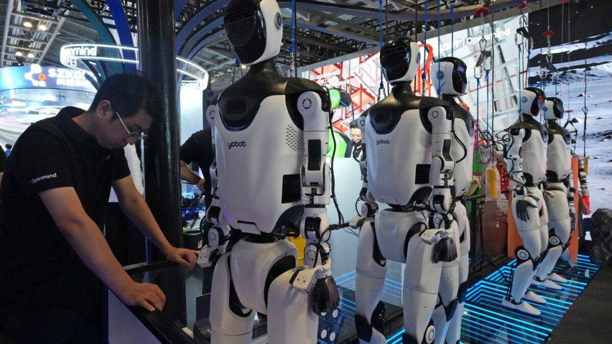 A worker reacts near a line of humanoid robots displayed at the World AI Conference in Shanghai.