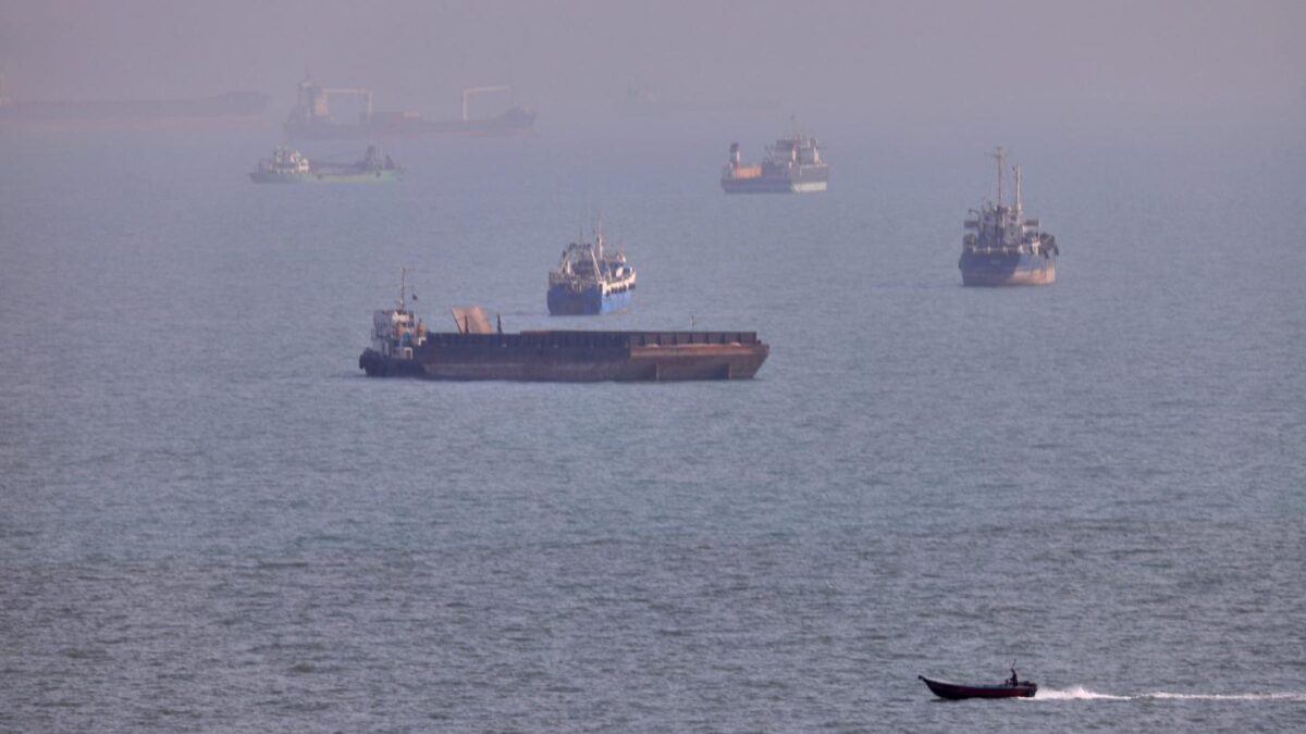A small boat sails past cargo ships and other commercial vessels anchored in the Strait of Hormuz off Bandar Abbas, Iran.