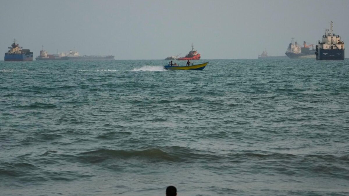 A swimmer remains near the shore as a motorboat passes commercial vessels anchored in the Strait of Hormuz off Bandar Abbas, Iran, Friday, Sept. 4, 2026.