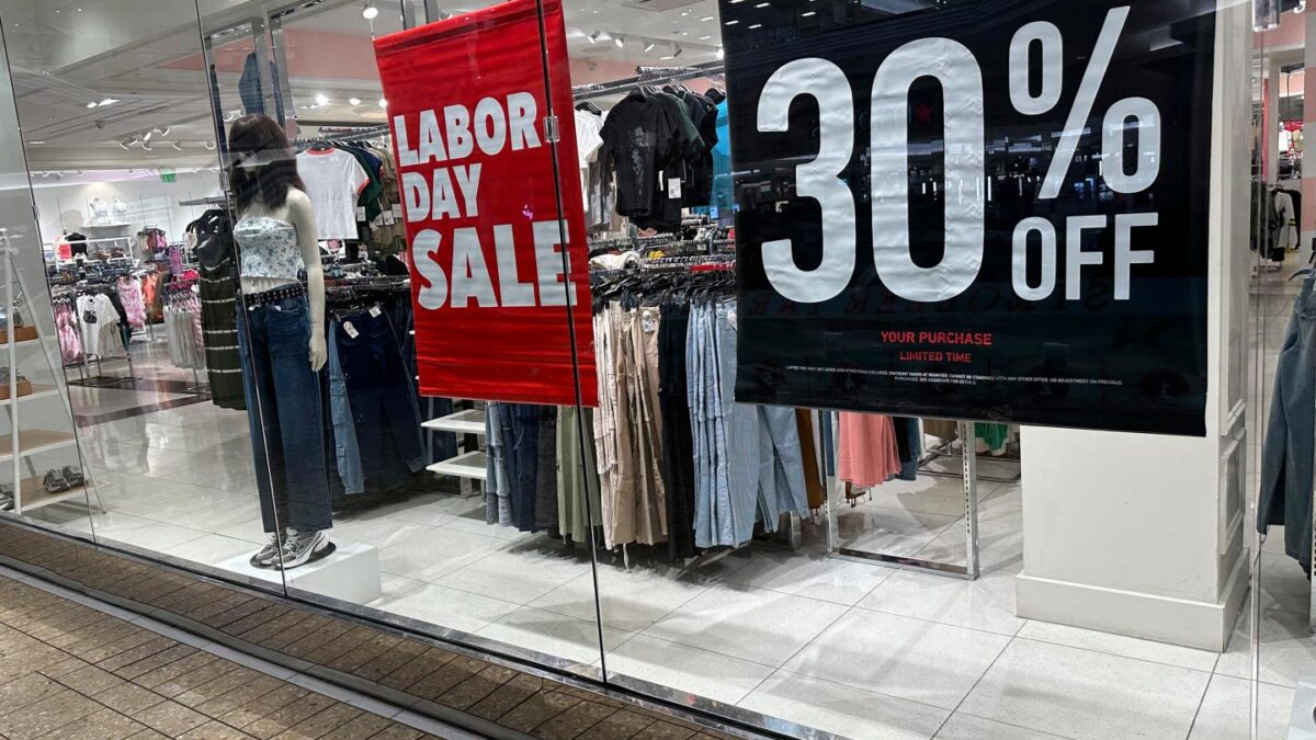 Signs announce a Labor Day sale in the window of a clothing store at a mall in Denver on Aug. 21, 2024.
