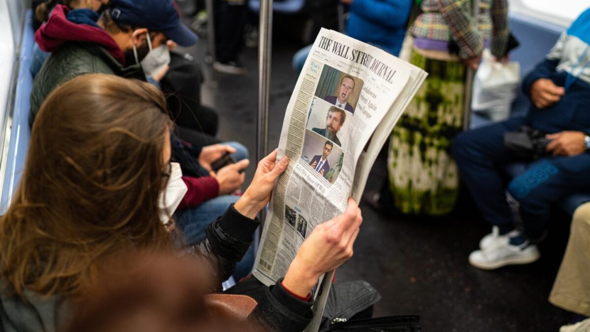 A woman reads the Wall Street Journal newspaper while sitting on the subway.