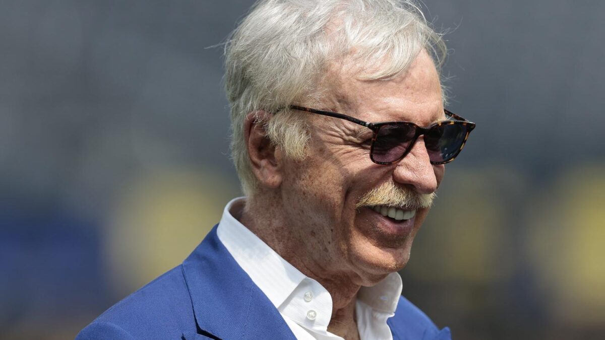 Stan Kroenke, wearing a blue suit and sunglasses, smiles.
