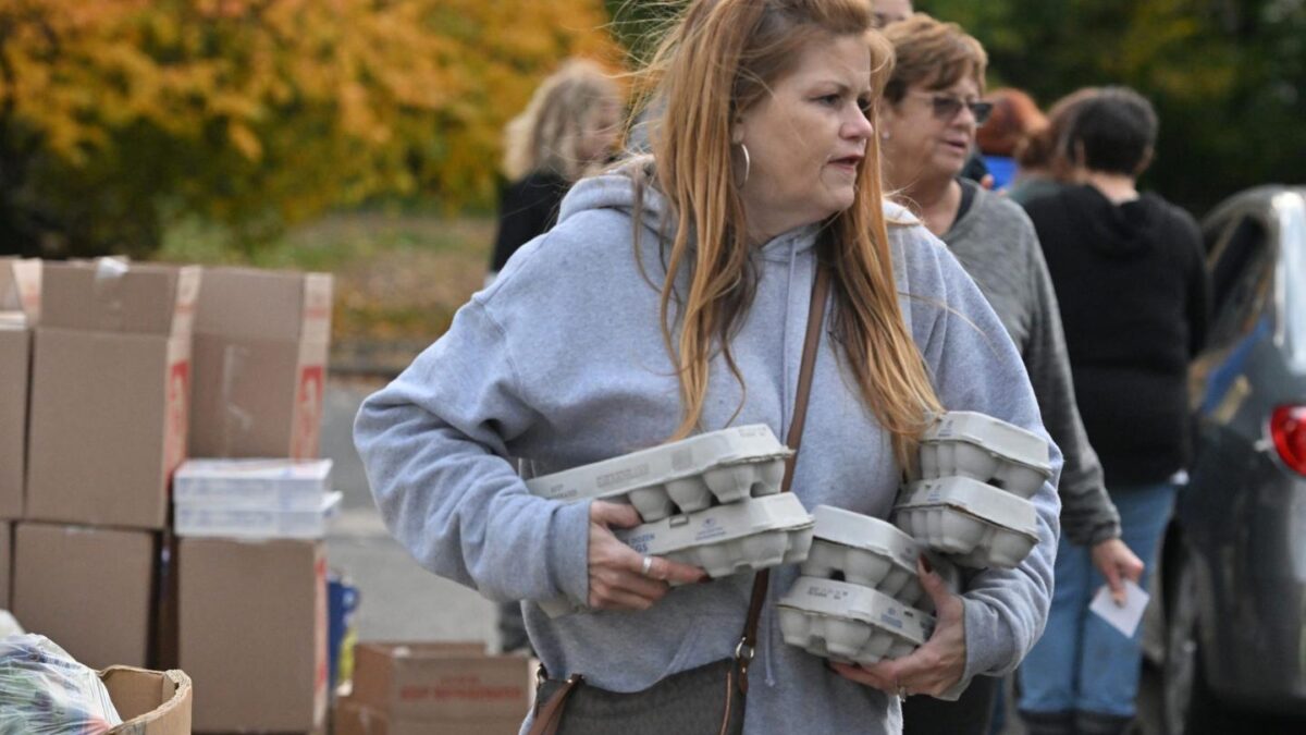 A woman in a grey hoodie holds six cartons of eggs in her arms.