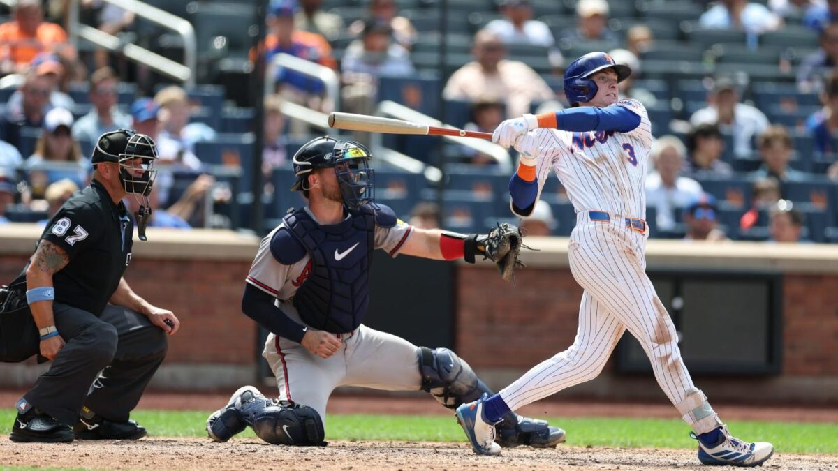 A baseball player swinging his bat with two umpires behind him.